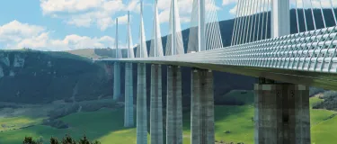 Moderne Bruecke ueber einem Tal vor Huegeln.