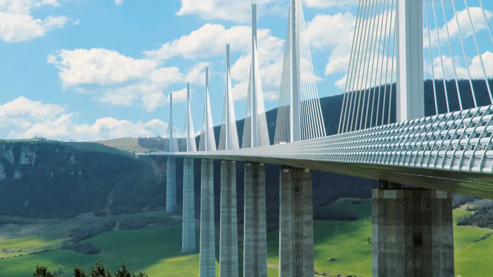 Moderne Bruecke ueber einem Tal vor Huegeln.