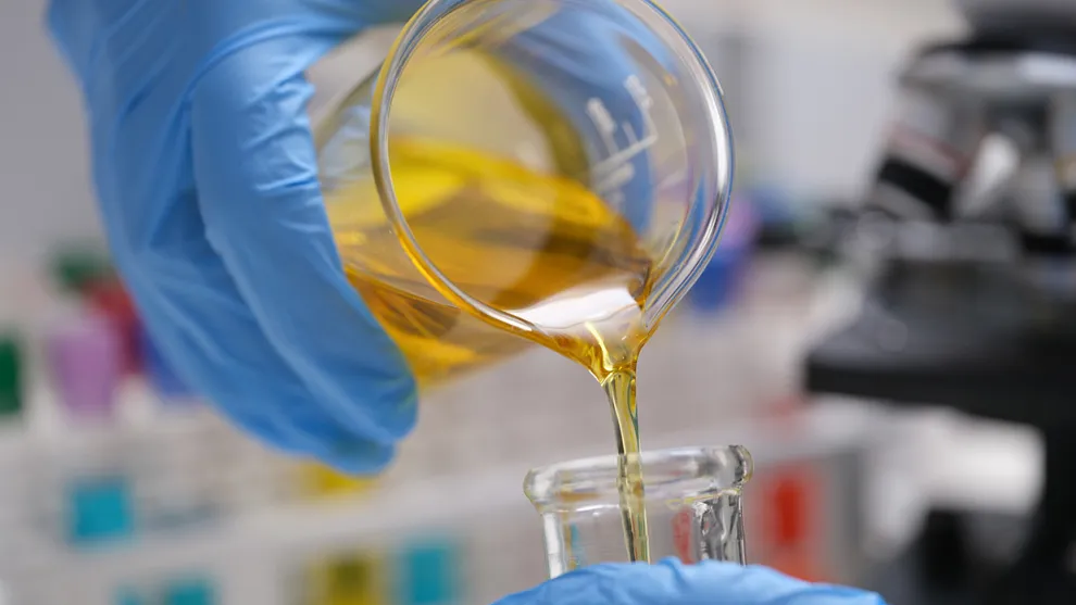 Gelbe Flüssigkeit wird aus einem Glasbehälter in einen anderen gegossen. 
