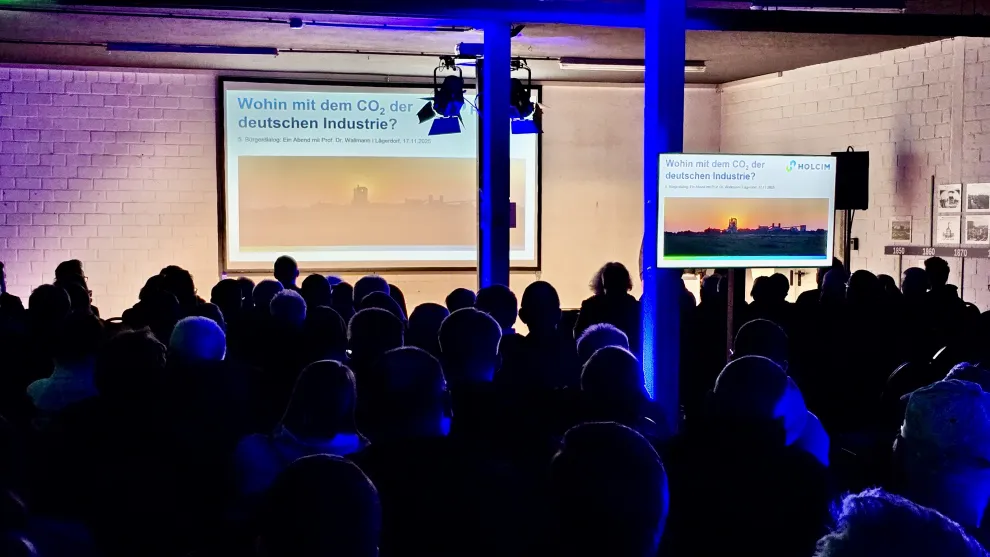 Abgedunkelter Vortragsraum mit Publikum von Hinten und einer Leinwand