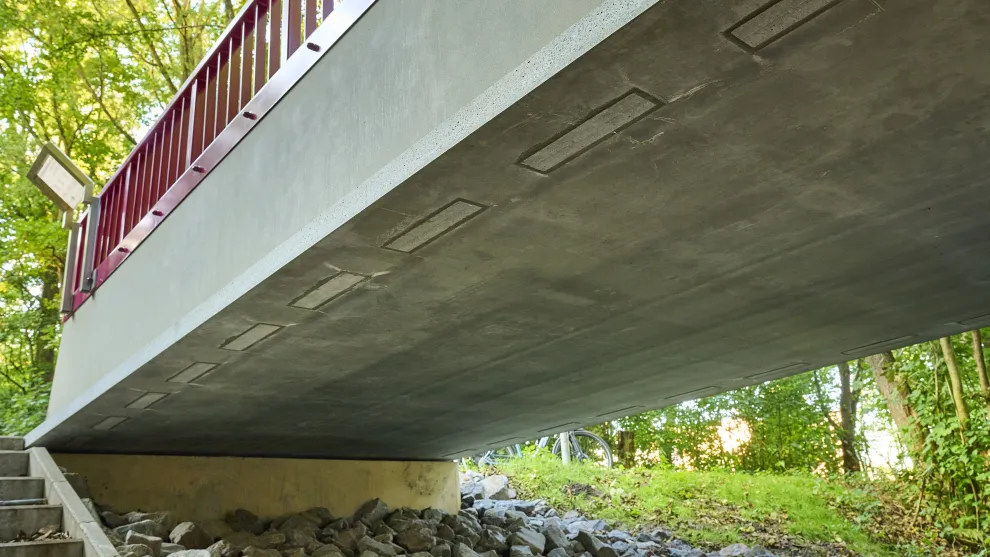 Brücke aus Carbonbeton von unten in einer grünen Umgebung.
