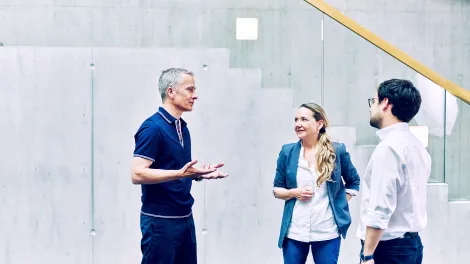 drei Personen unterhalten sich angeregt vor einer Treppe.