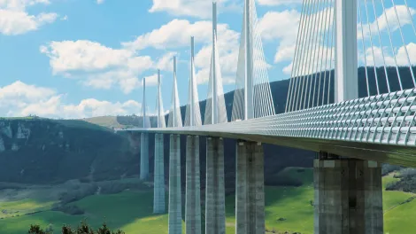 Moderne Bruecke ueber einem Tal vor Huegeln.