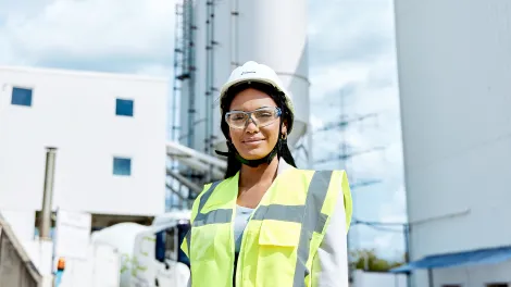 Junge Frau mit Warnweste und Anstoßkappe in einem Betonwerk.
