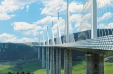 Moderne Bruecke ueber einem Tal vor Huegeln.