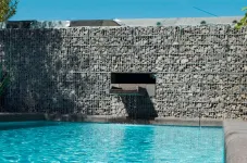 Mauer aus Gabionsteinen mit einem Wasserelement, dass in einen Pool plätschert.